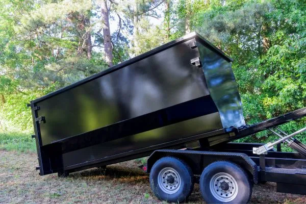 black dumpster rolling off from the back of a truck surrounded by trees