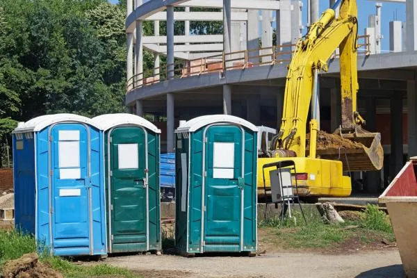 three blue and green portable toilets next to excavator on construction site