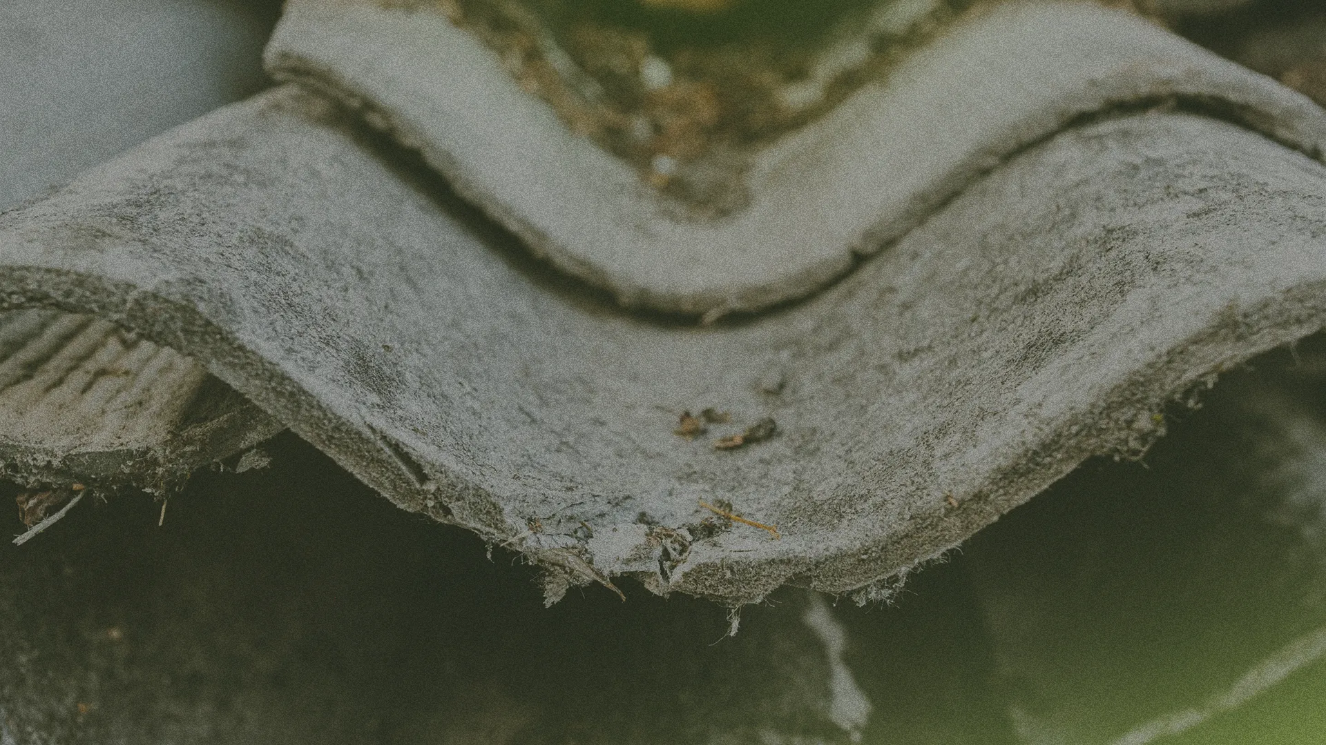 Close-up of weathered, overlapping roof tiles with visible moss and dirt, creating a textured and aged appearance.