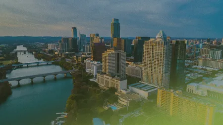 Aerial view of a city skyline at dusk with tall buildings, a river, and multiple bridges extending into the distance.