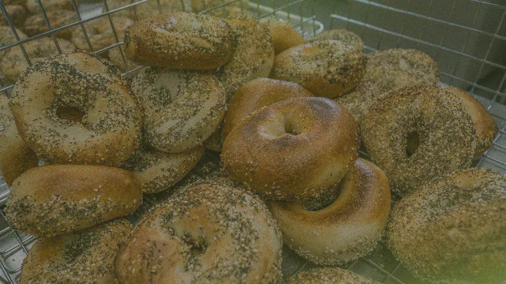 A wire basket filled with a variety of bagels, some topped with sesame and poppy seeds.