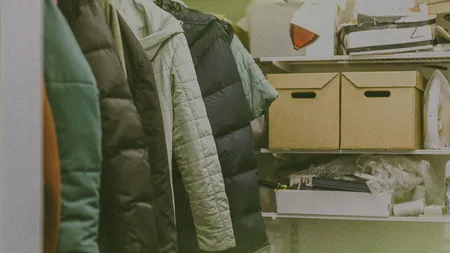 Coats hanging in a closet next to shelves with cardboard boxes and various items.