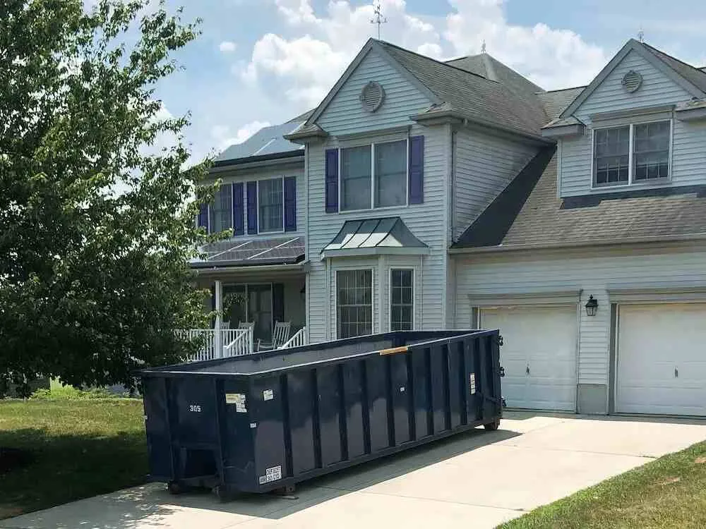 A picture of dumpster in front of a grey house 