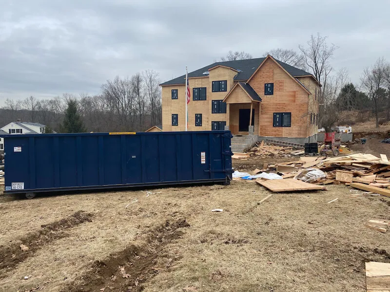 Roll off bin on a construction site in front of house under construction.