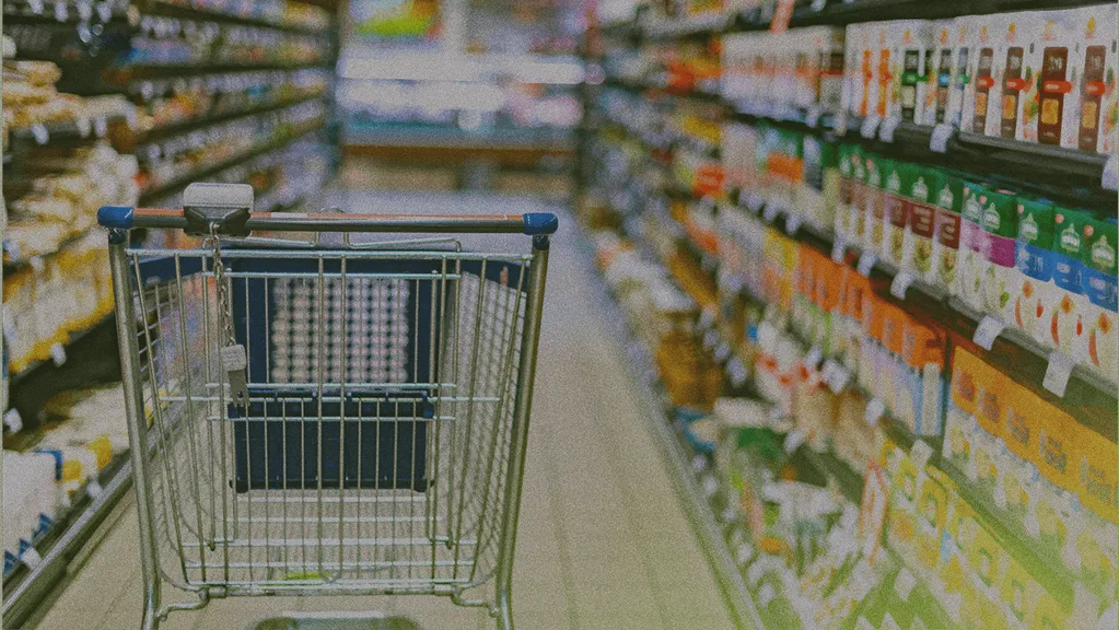 Shopping cart in a supermarket aisle, surrounded by shelves stocked with various products and colorful packaging.