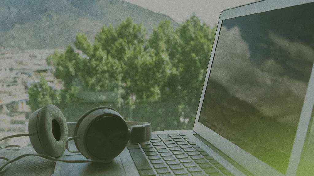 Laptop and headphones on a table with a blurred view of mountains and trees in the background.