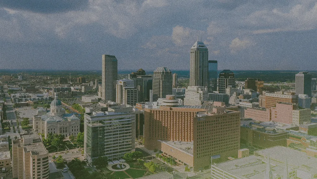 Aerial view of a city skyline with tall buildings under a partly cloudy sky, featuring a mix of modern and historic architecture.