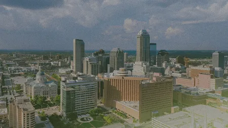 Aerial view of a city skyline with tall buildings under a partly cloudy sky, featuring a mix of modern and historic architecture.