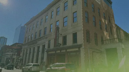 Street view of a historic three-story brick building with cars parked along the sidewalk and a sign reading "LOOKOUT" on the corner.