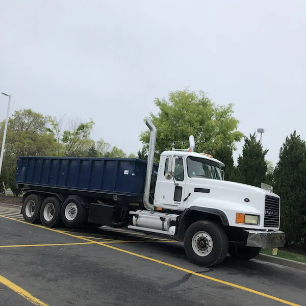 Dumpster truck in parking lot with trees behind it 