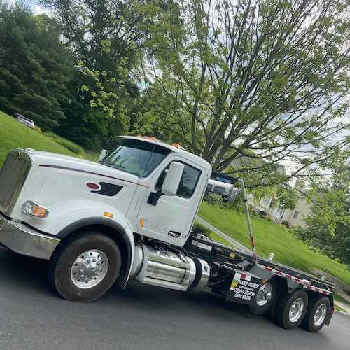 Roll off dumpster rental truck on the street under a green tree