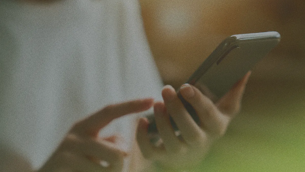 Person holding a smartphone with both hands, using their index finger to interact with the screen in a softly blurred background.