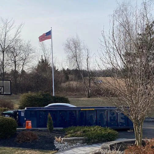 Picture of blue dumpster underneath an American flag