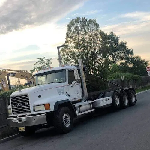 Roll off dumpster rental truck in sunset with machine in background