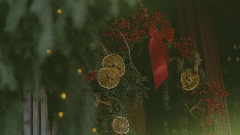 holiday wreath on a front door decorated with a red bow and orange slices